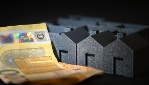 Close-up of black miniature houses with Euro notes, representing real estate investment and savings.
