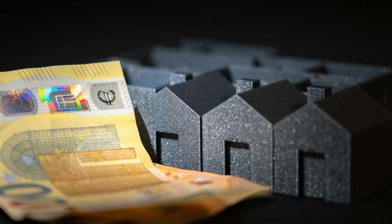 Close-up of black miniature houses with Euro notes, representing real estate investment and savings.